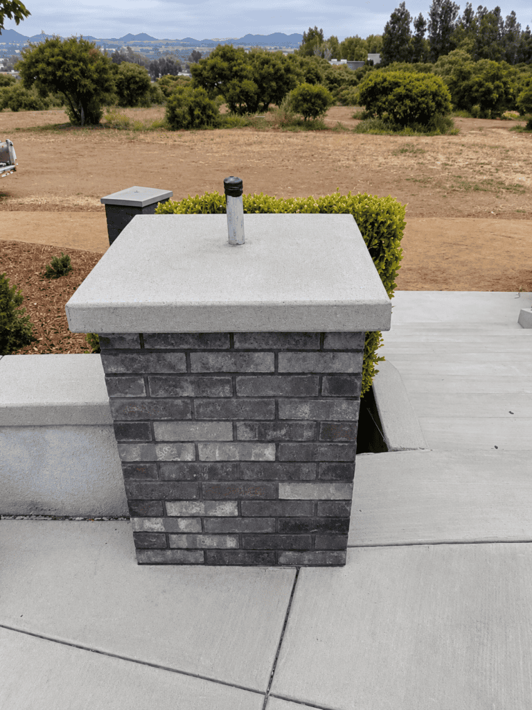 Concrete chimney with brick base on rooftop with scenic landscape background.