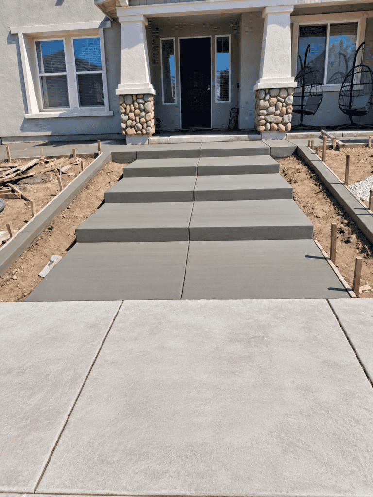 Modern concrete walkway leading to a residential front door with steps and landscaping.