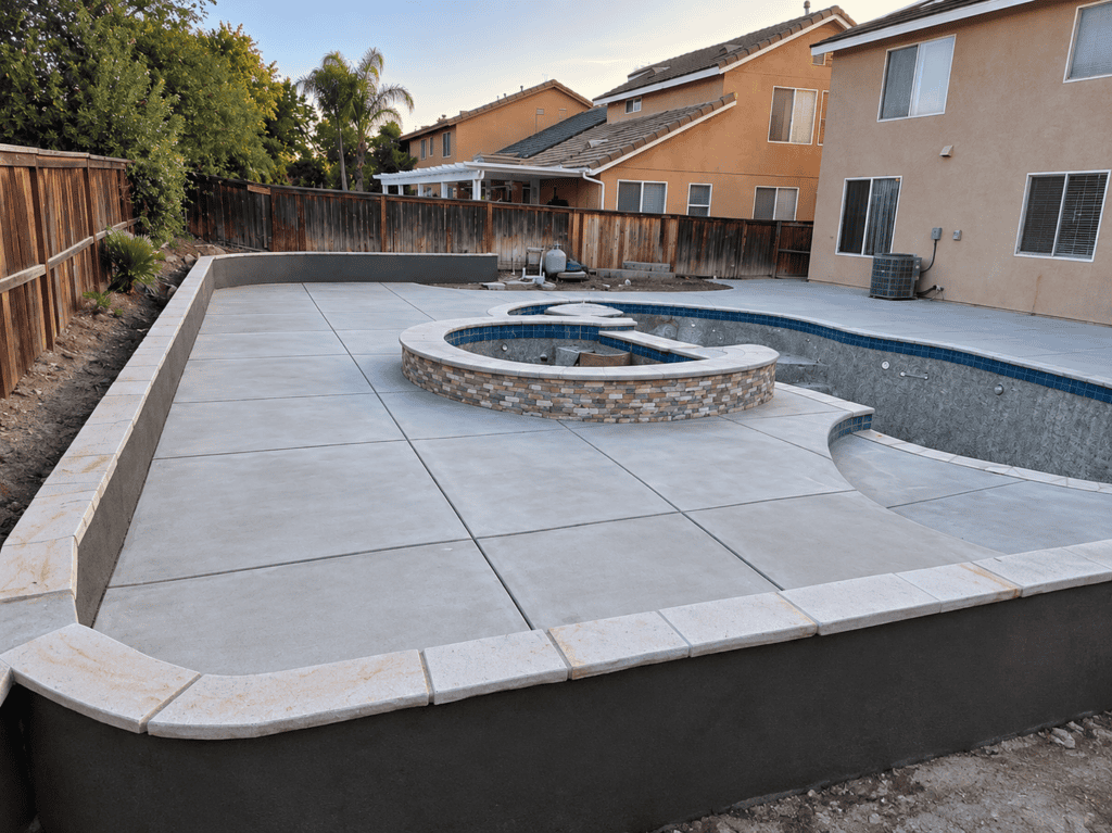 Concrete pool with built-in spa and surrounding patio in backyard.