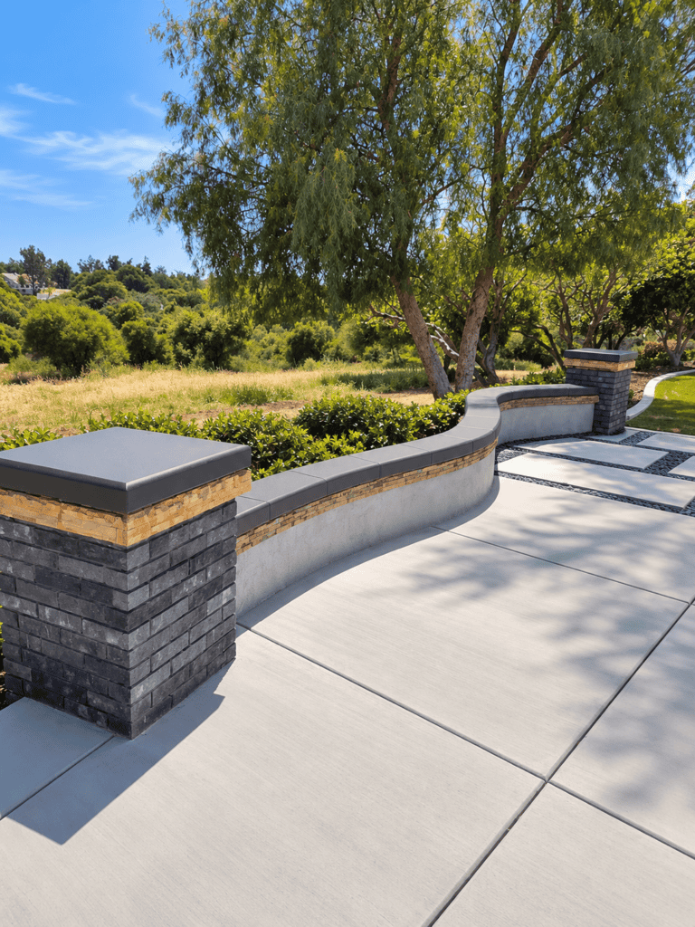 Contemporary concrete patio with decorative wall and lush landscape background.