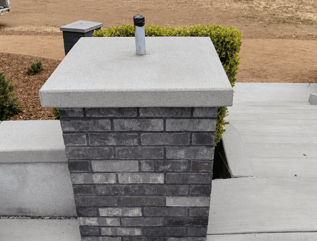 Concrete chimney with brick base on rooftop with scenic landscape background.