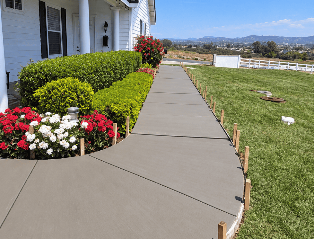 Newly poured concrete sidewalk with wooden stakes in front of a white house.