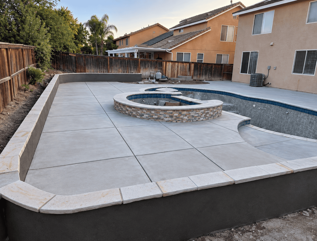 Concrete pool with built-in spa and surrounding patio in backyard.