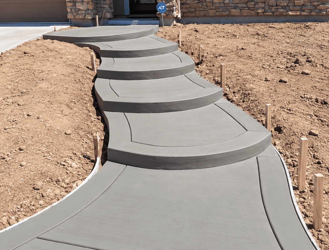 Curved concrete walkway leading to house entrance with landscaping.